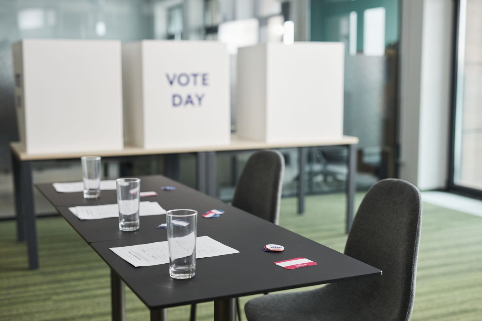 Sala preparada para votação, com mesas, cadeiras e cabines de privacidade organizadas.