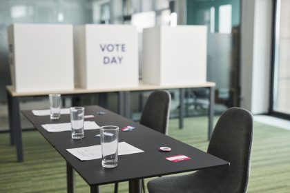 Sala preparada para votação, com mesas, cadeiras e cabines de privacidade organizadas.