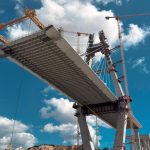 Ponte em construção com guindastes contra o céu azul.