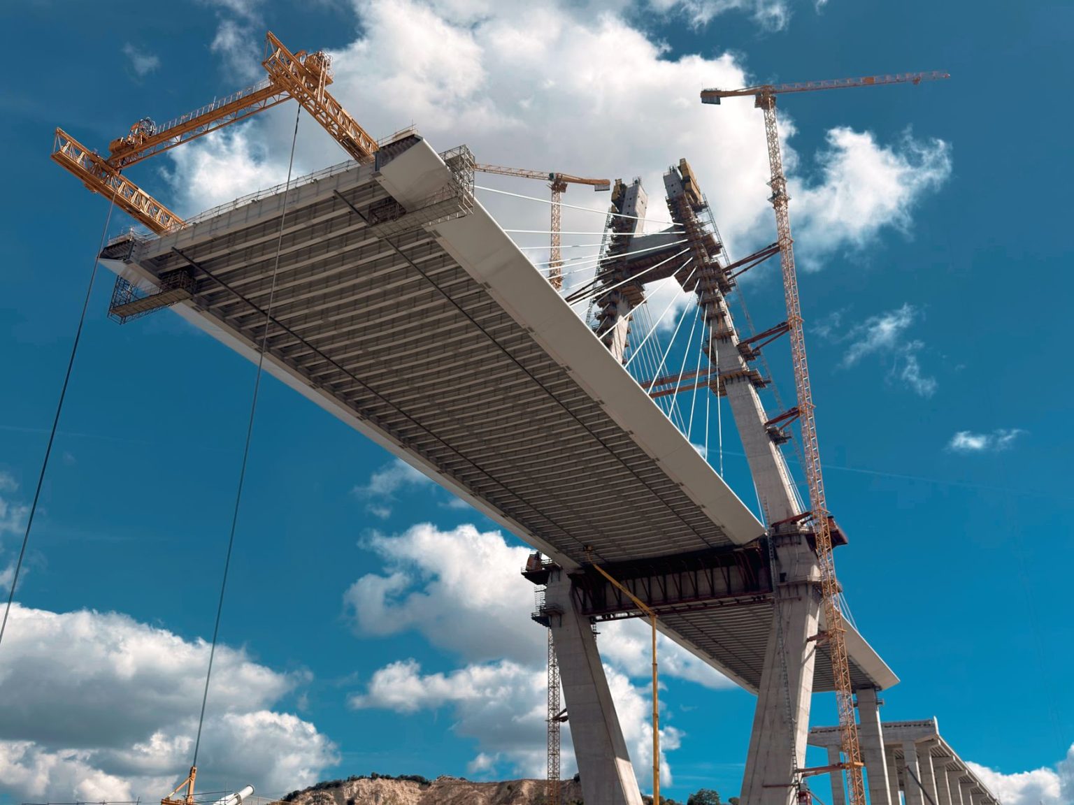 Ponte em construção com guindastes contra o céu azul.