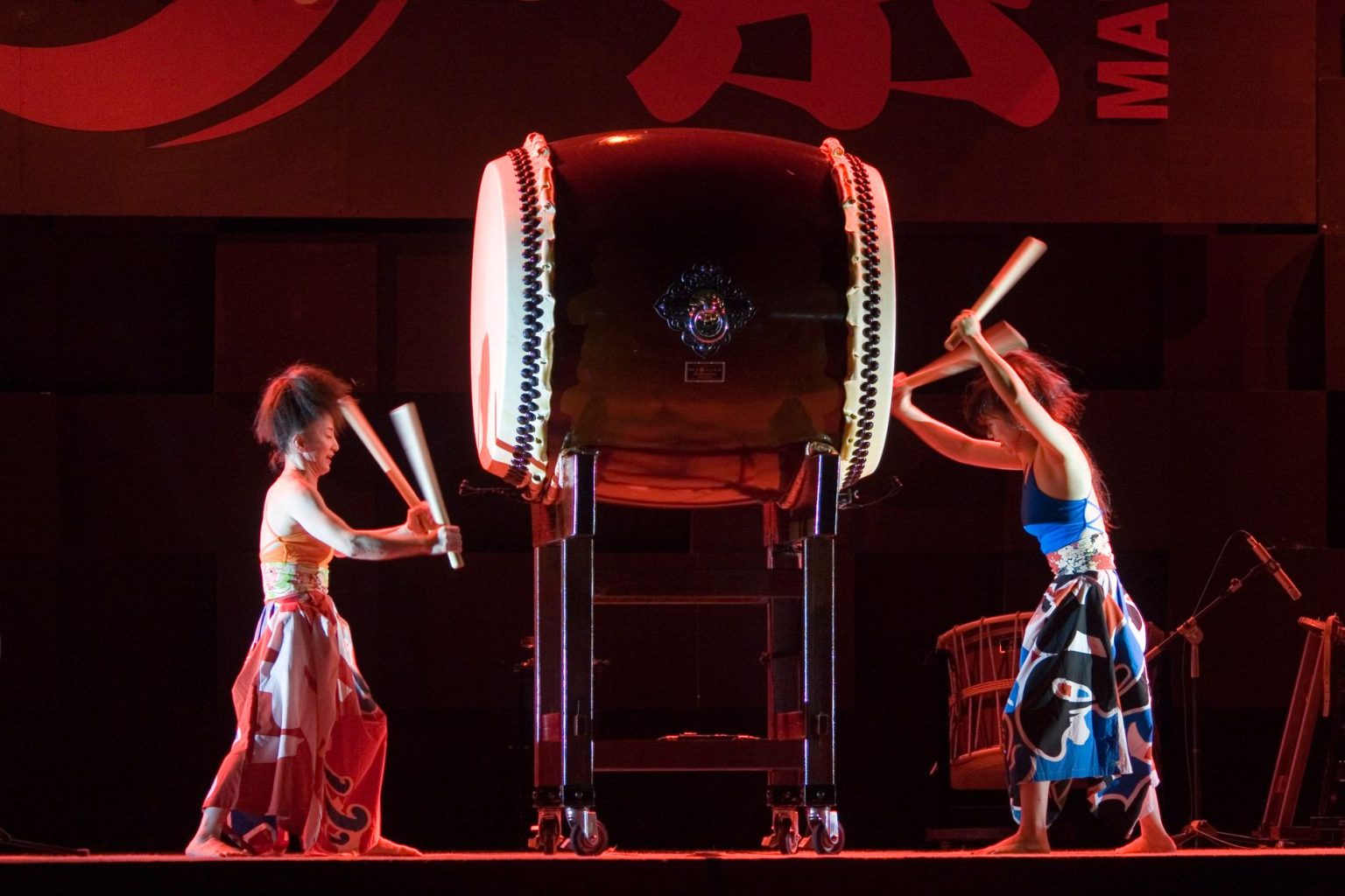 Músicos usando trajes tradicionais japoneses tocam tambores taiko durante uma apresentação em um palco.