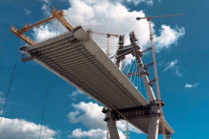 Ponte em construção com guindastes contra o céu azul.