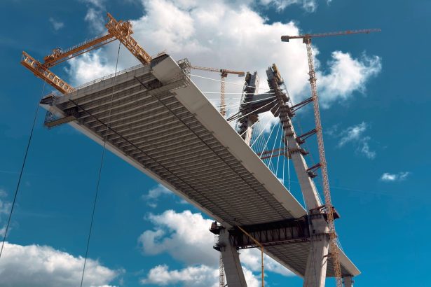 Ponte em construção com guindastes contra o céu azul.