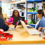 Grupo diverso de estudantes participa de uma atividade prática e colaborativa em um ambiente de oficina.