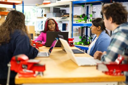Grupo diverso de estudantes participa de uma atividade prática e colaborativa em um ambiente de oficina.