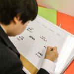 Pessoa organiza um planejamento semanal em uma agenda sobre a mesa de trabalho.