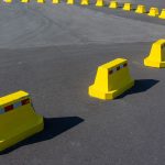 Fileira de barreiras amarelas bloqueia uma via urbana asfaltada.