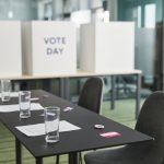 Seção eleitoral organizada em uma sala, com mesas, cadeiras e cabines de votação.