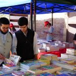 Pessoas observam e manuseiam livros em uma feira literária ao ar livre.