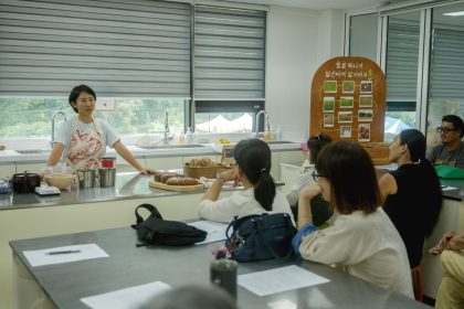 Instrutor orienta uma turma diversa de adultos durante uma aula de culinária em uma cozinha.