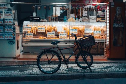 Bicicleta estacionada diante de uma loja iluminada em Curitiba, com produtos expostos na fachada.